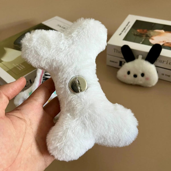 White plush toy with a button held by a hand on a brown surface with books in the background.