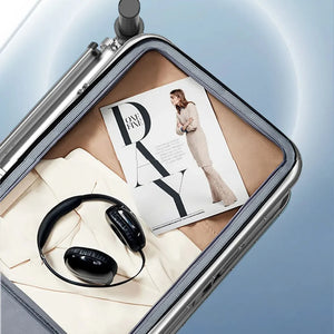 A silver hard-shell suitcase shown open on a light blue gradient background, with interior accessories including a black pair of headphones, a magazine, and folded cream bedding or fabric. Chinese marketing text appears at the top, and the brand name LVSHANGMEI is visible in the upper left.