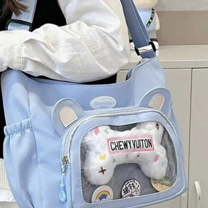 Light blue pet carrier with a plush toy labeled 'CHEWY VUITON' inside, held by a person.